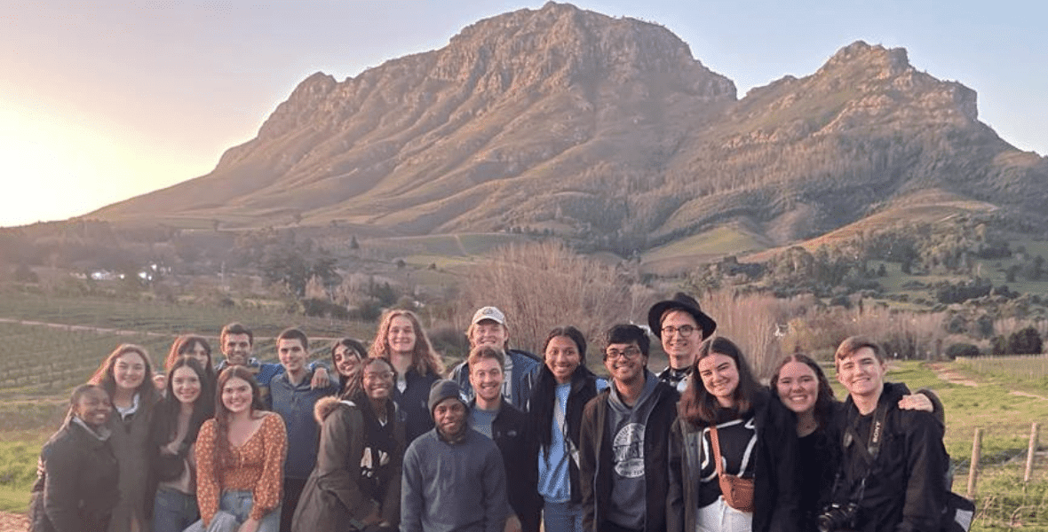 A group of scholars pose for a photo with mountains in the background in South Africa.
