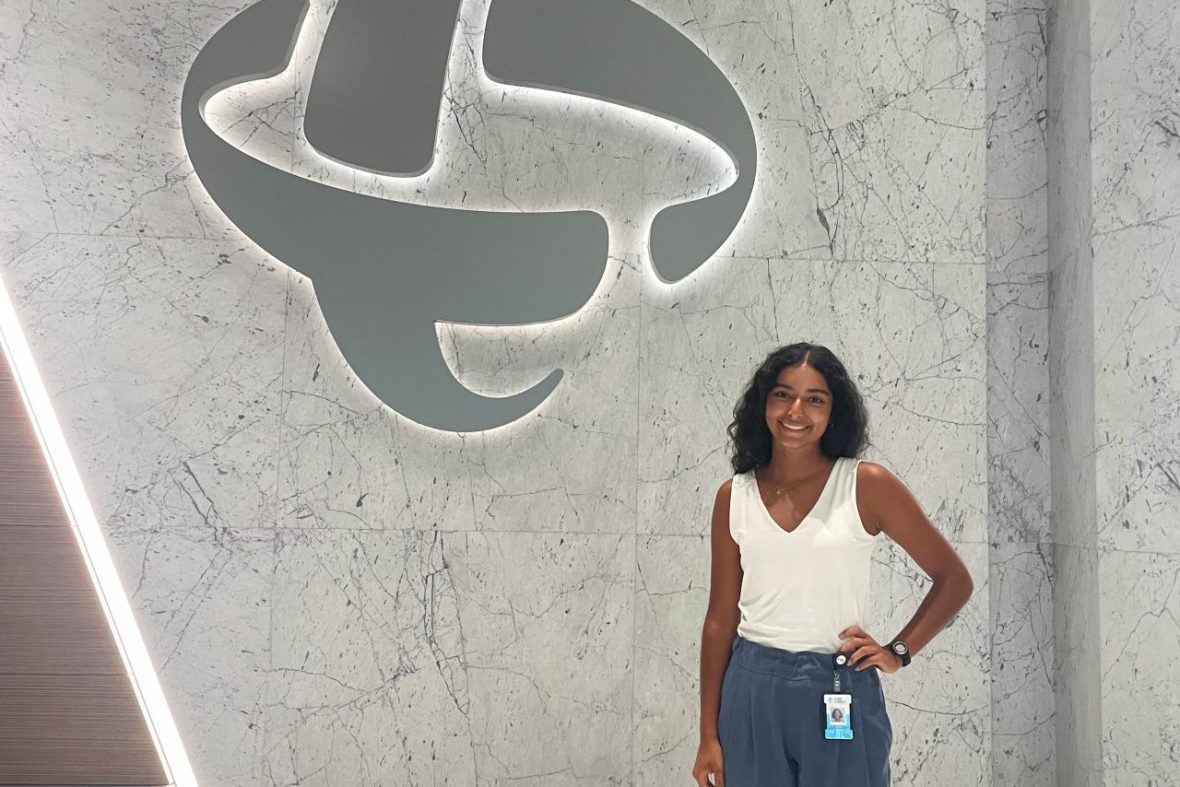 A scholar standing in front of the Duke Energy logo at their uptown headquarters.