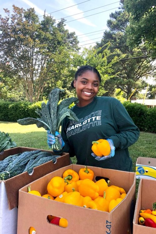 A scholar poses for a photo while handing out vegetables for civic engagement project.